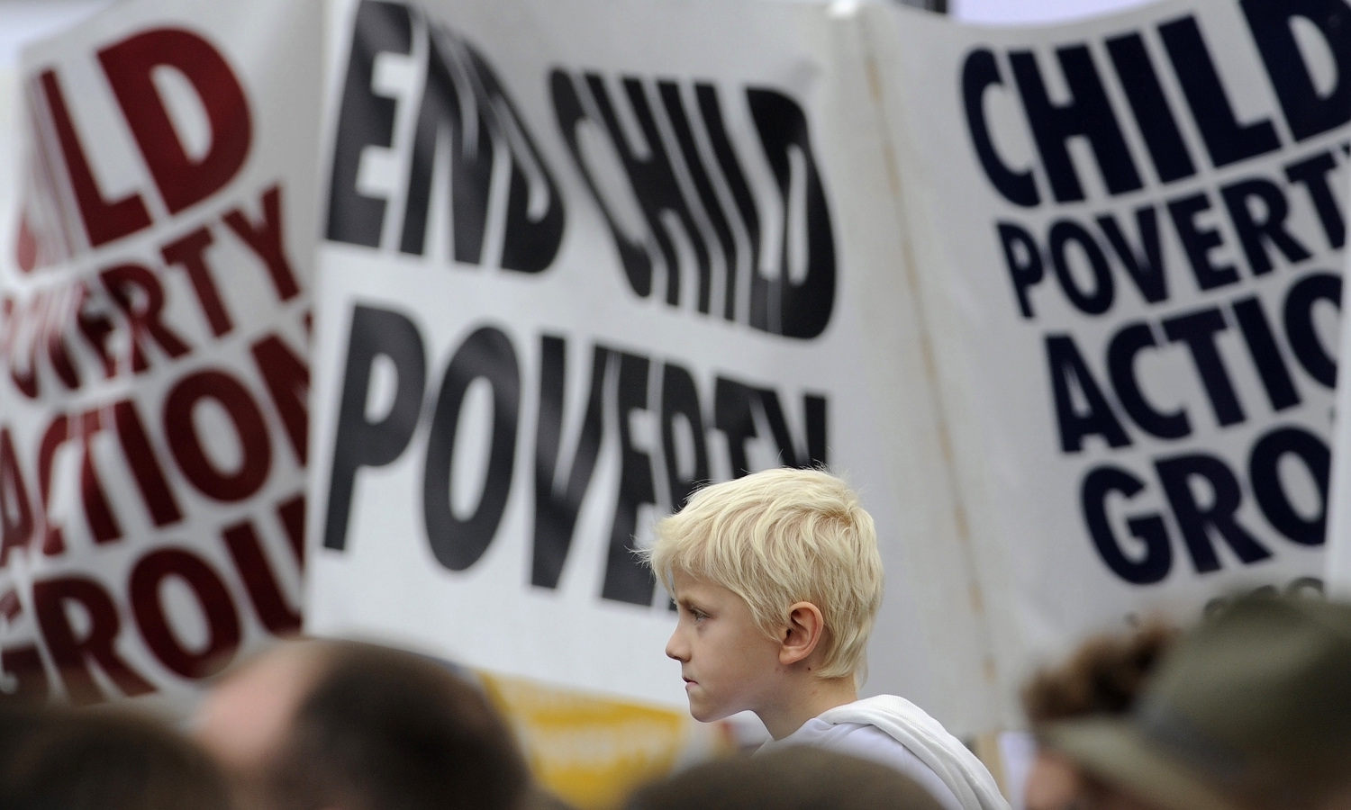 A junior-aged boy's profile is seen against a backdrop of banners reading 'End Child Poverty'